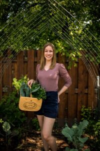 Photo of our speaker,  Nicole Jagelieski., standing in a garden holding a basket.